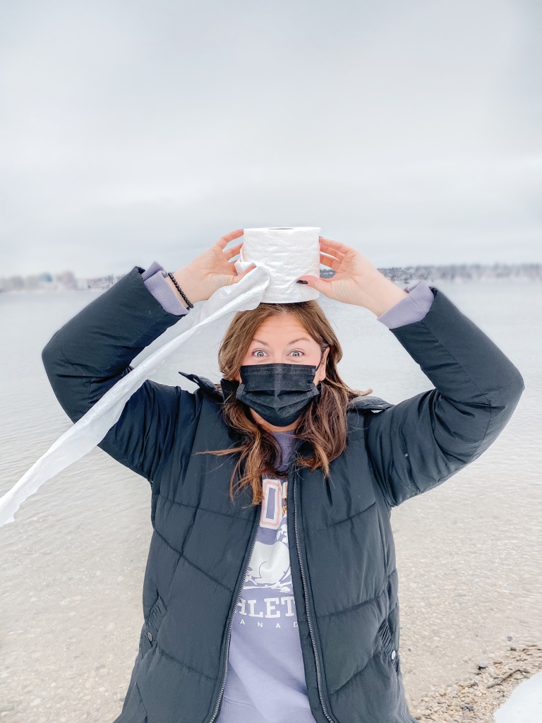 Woman wearing a mask and holding a roll of toilet paper on her head